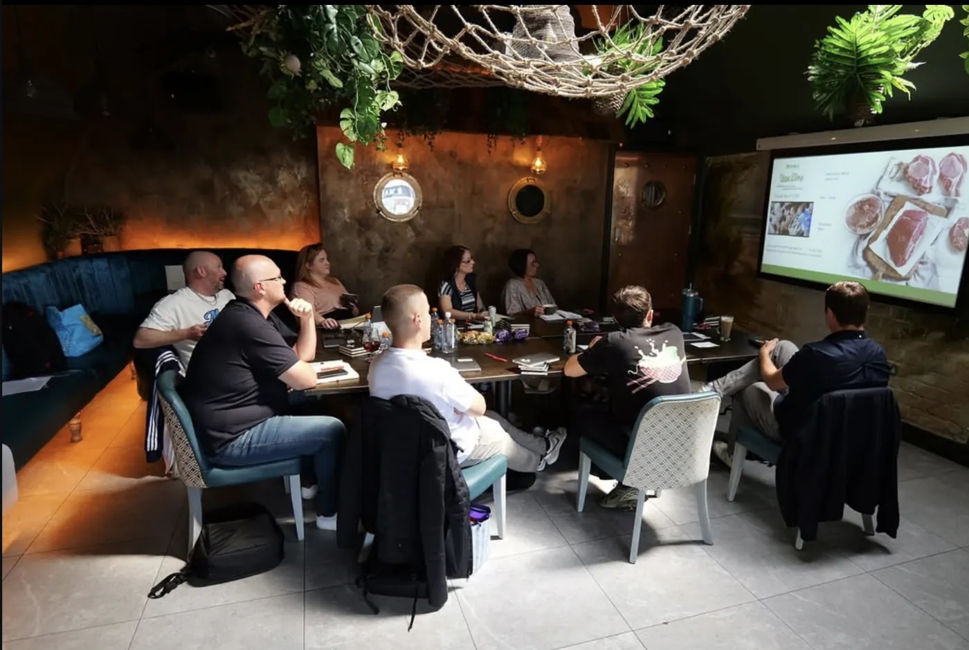 A morning meeting around a long table facing the screen